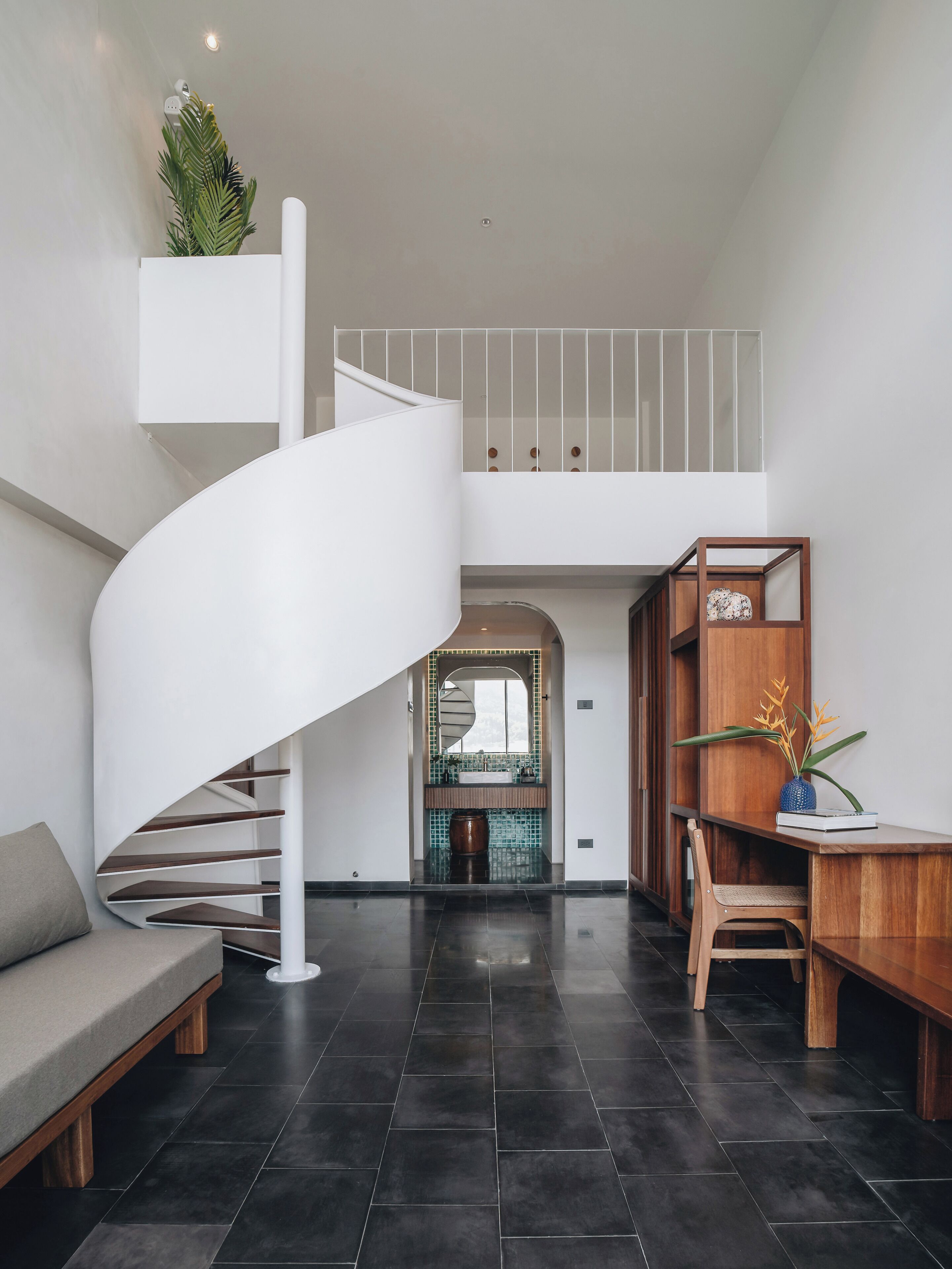 Un intérieur moderne avec un escalier en colimaçon, un bureau en bois, un banc et, au fond, un coin cuisine.