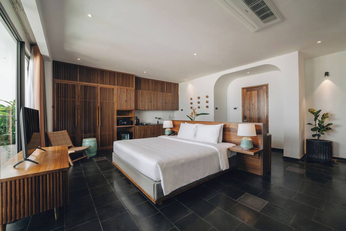 A modern hotel room with a large bed, wooden furniture, a desk, and a view of the outdoors.
