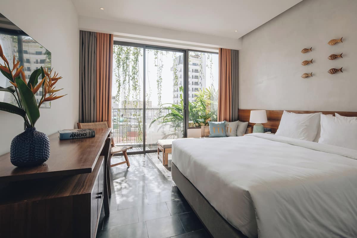 A hotel room with a large bed, a desk with a vase, and a view of the city.