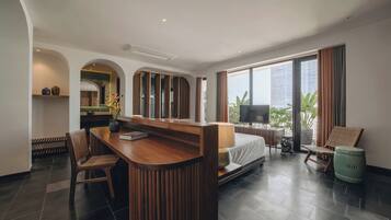A modern hotel room with a wooden desk, a bed, a TV, and a view of the city.