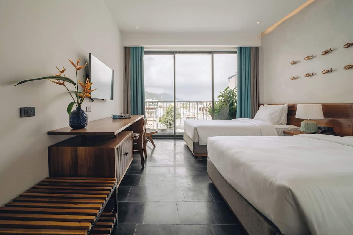 A hotel room with a bed, a desk, a chair, a TV, and a view of the outdoors.