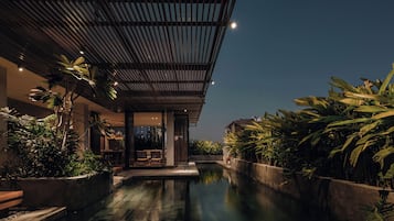 A modern hotel with a pool, surrounded by lush greenery and a covered outdoor area.