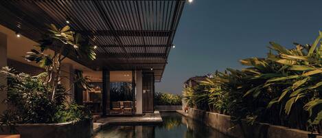 A modern hotel with a pool, surrounded by lush greenery and a covered outdoor area.