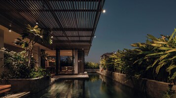 A modern hotel with a pool, surrounded by lush greenery and a covered outdoor area.