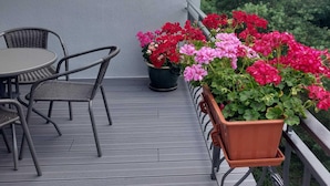 A balcony with a table and chairs, potted plants with red and pink flowers, and a railing. - Apartment in Sopot Near Monte Cassino Street (Sopot)
