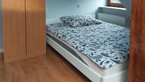 A bedroom with a wooden wardrobe, a bed with patterned bedding, and a radiator. - Apartment in Sopot Near Monte Cassino Street (Sopot)