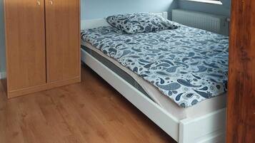 A bedroom with a wooden wardrobe, a bed with patterned bedding, and a radiator.