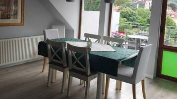 A dining area with a table set for four, white chairs, and a view of a balcony with greenery.