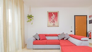 A modern living room with a sectional sofa, a hanging plant, a framed artwork, and a fire extinguisher on the wall. - Girasole (A5) | Three-room apartment with two bathrooms | Rho Fiera | Malpensa | Milan (Cesate)