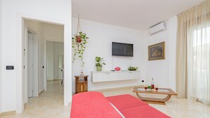 A modern living room with a red sofa, a wooden coffee table, a TV mounted on the wall, and a potted plant. - Girasole (A5) | Three-room apartment with two bathrooms | Rho Fiera | Malpensa | Milan (Cesate)
