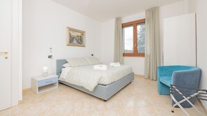 A bedroom with a bed, a nightstand, a chair, a window with curtains, and a painting on the wall. - Girasole (A5) | Three-room apartment with two bathrooms | Rho Fiera | Malpensa | Milan (Cesate)