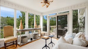 A sunlit room with large windows, a wooden deck, a white sofa, and a table with decorative items. - Sonny Pointe On the Creek, Steps away from the Beach, Pet Friendly (Georgetown)