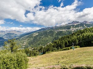 A mountainous landscape with a ski lift, lush greenery, and a clear sky.