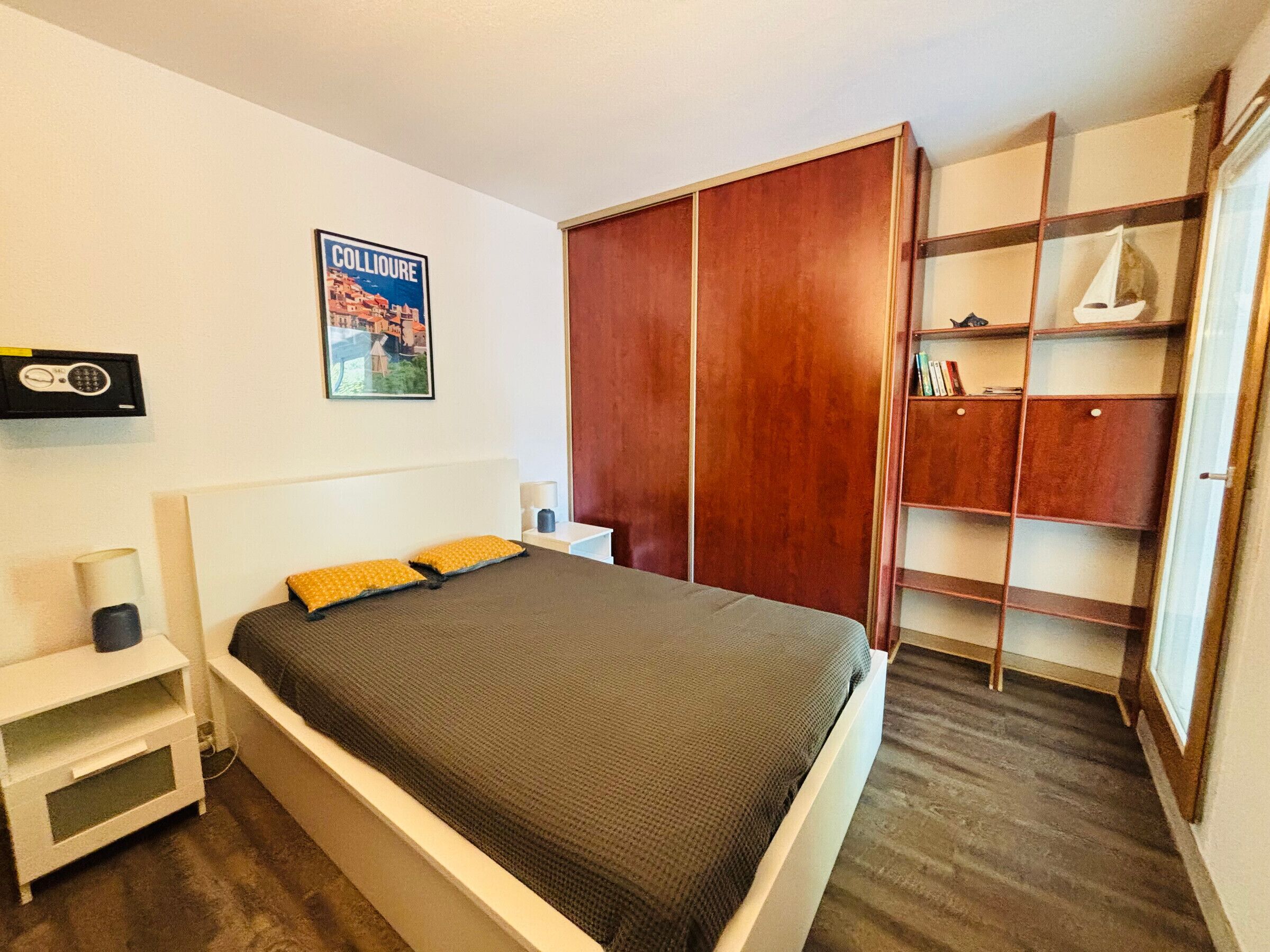 Een slaapkamer met een bed, een kledingkast, een nachtkastje en een poster aan de muur.