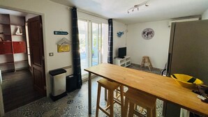 Un ambiente compatto con un tavolo di legno, due sedie, un piccolo televisore e un frigorifero.