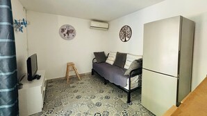 Una stanza piccola e compatta con un pavimento decorato, un letto con cuscini, un tavolino con un televisore, una scala e un frigorifero.