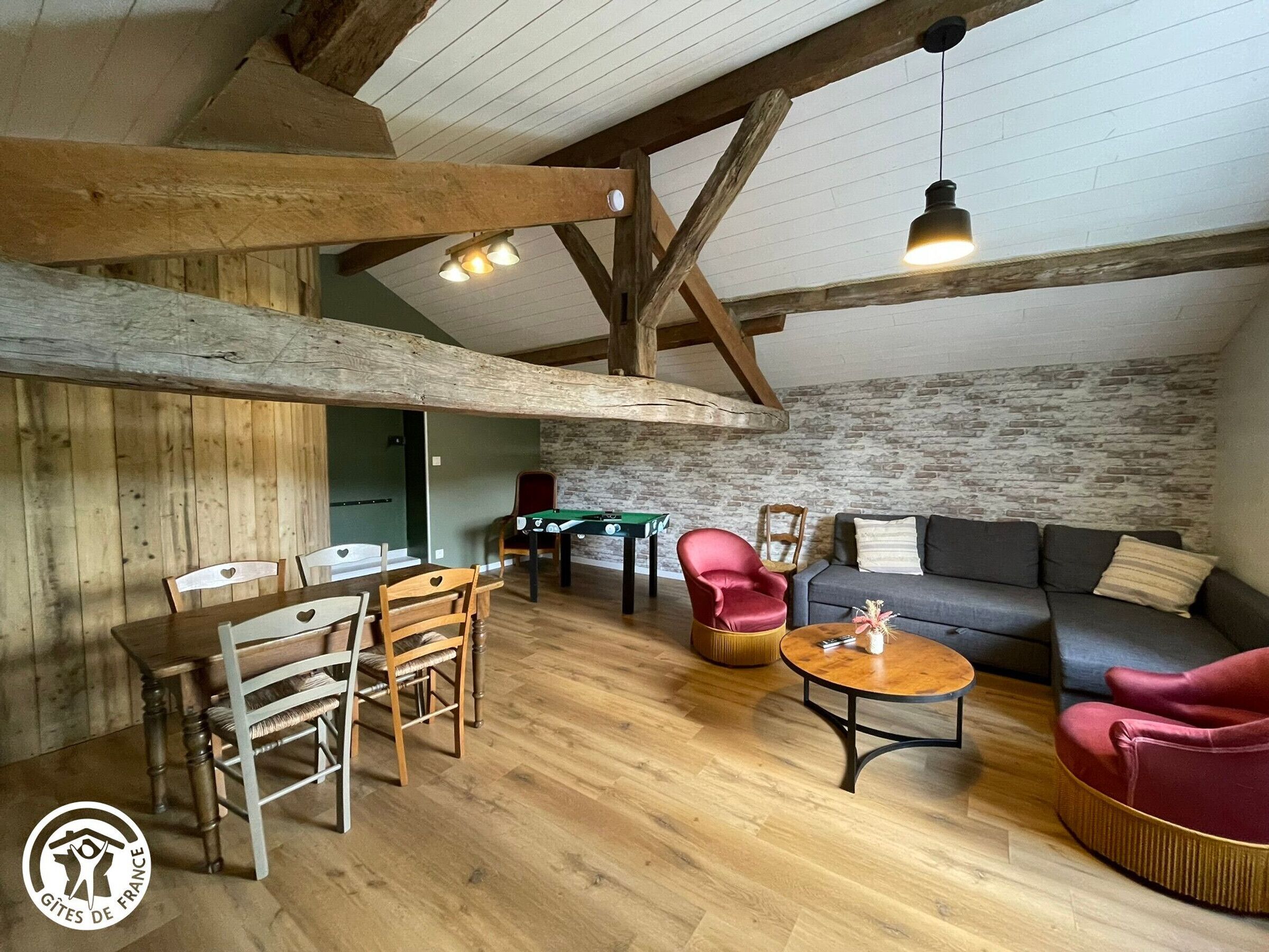 Une pièce chaleureuse de style loft, avec des poutres apparentes, une table de billard, un canapé et une table basse.