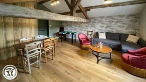Une pièce chaleureuse de style loft, avec des poutres apparentes, une table de billard, un canapé et une table basse.