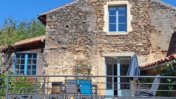 Une maison en pierre dotée d’un balcon, avec une rambarde en métal et une terrasse en bois.