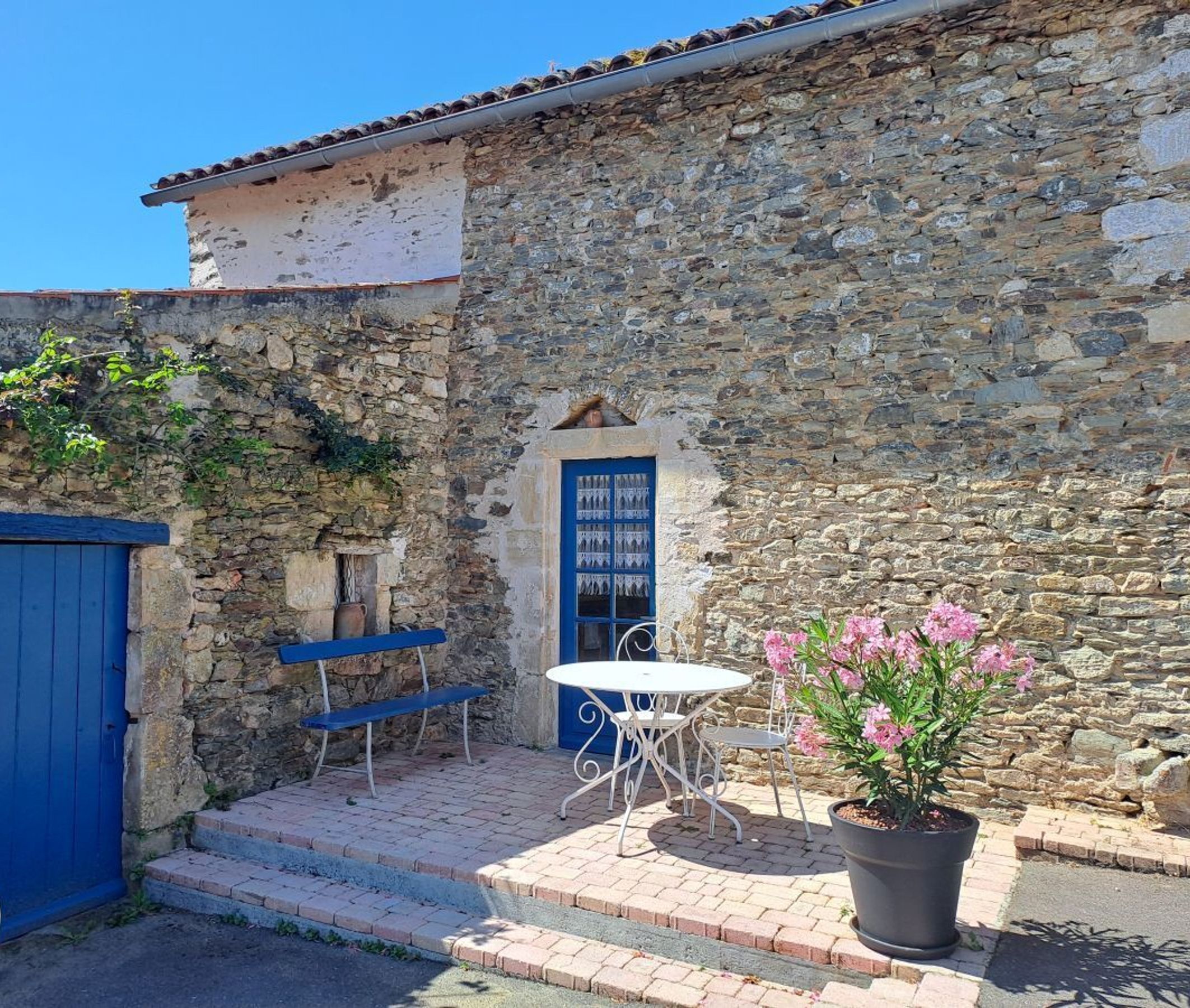 A stone building with a blue door, a small window, and a table with chairs outside.