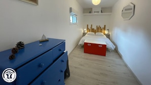 Ein Schlafzimmer mit einem Bett, einem Schminktisch, einem kleinen Fenster und einer Wandleuchte.