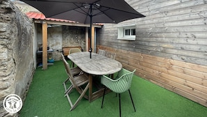 Eine Terrasse mit Tisch, Stühlen und einem Sonnenschirm, sowie ein kleines Fenster.