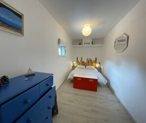 A bedroom with a bed, a dresser, a small window, and a wall-mounted light fixture. - Air-conditioned house near the beach in Saint-Hilaire-de-Riez (Saint-Hilaire-de-Riez)