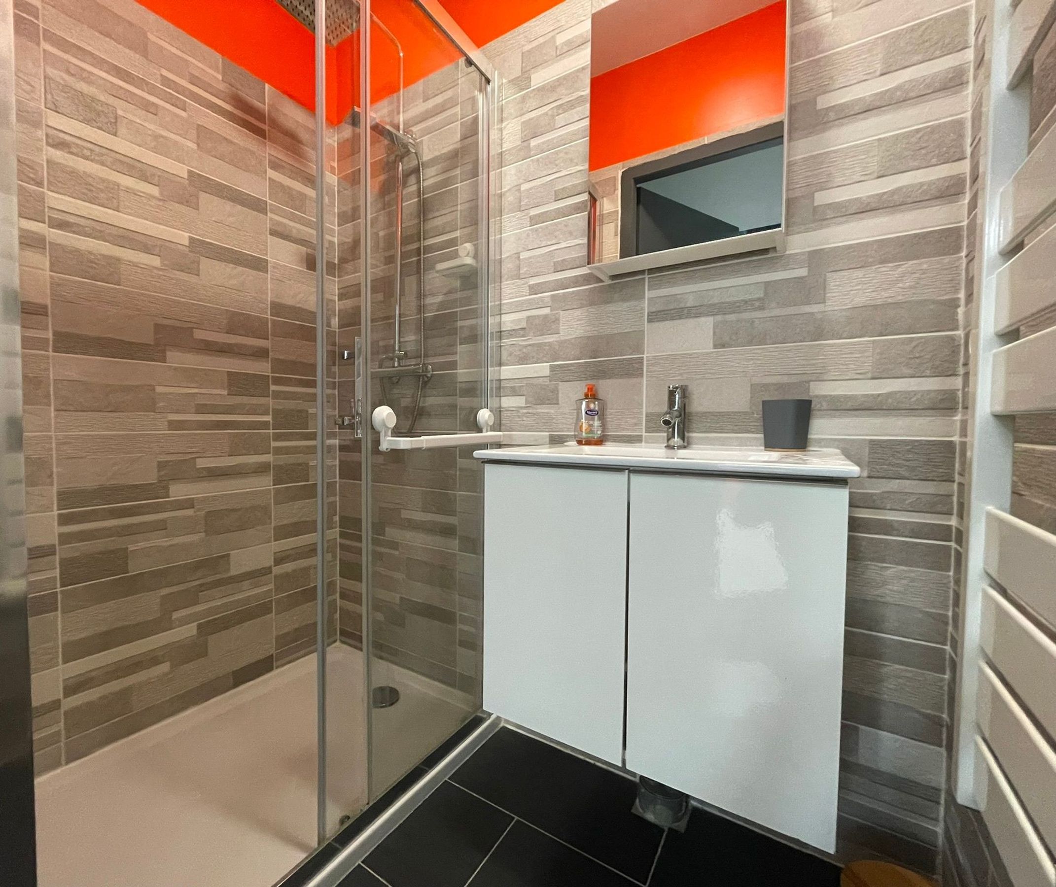 A modern bathroom with a glass-enclosed shower, a white vanity with a mirror, and a tiled wall with a wood-like pattern.