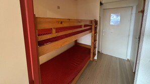 A bunk bed with red bedding in a hallway with a white door and a small window. - Studio cabin 4 pers. in L'Alpe d'Huez with balcony (Huez)