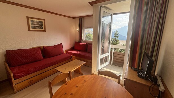 A cozy room with a wooden sofa, a small table, and a balcony with a view of mountains. - Studio cabin 4 pers. in L'Alpe d'Huez with balcony (Huez)