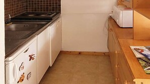 Cocina compacta con armarios blancos, estufa negra, microondas y encimera de madera.