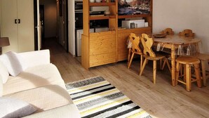 Un espacio habitable compacto con sofá, una mesa de comedor con sillas, un armario de madera y una alfombra estampada.