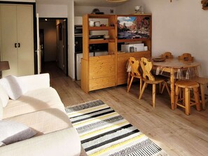 Un ambiente compatto con divano, tavolo da pranzo con sedie, un mobiletto in legno e un tappeto decorato.