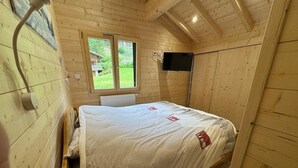 Une pièce de cabane en bois comprenant un lit, une fenêtre, un téléviseur fixé au mur et un radiateur.
