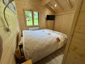 A wooden cabin room with a bed, a window, a mounted TV, and a radiator.