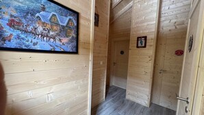 Un couloir intérieur en bois, orné d’un tableau représentant un paysage enneigé, avec une porte sur laquelle est apposée une pancarte et un interrupteur sur le mur.