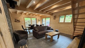 L’intérieur d’un chalet en bois chaleureux et accueillant, avec un canapé, des fauteuils, une table à manger et un escalier.