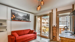 A modern living room with a red sofa, wooden flooring, a large window with a view of a building, and a painting on the wall.