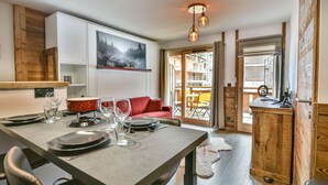 A modern dining area with a table set for four, a red sofa, and a view of the outside through a glass door.