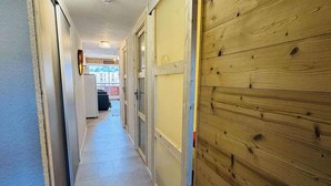 A narrow hallway with a tiled floor, wooden paneling on one side, and a door leading to a room with a window.