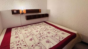 A bedroom with a bed, a headboard with built-in shelves, and a quilt with a geometric pattern.