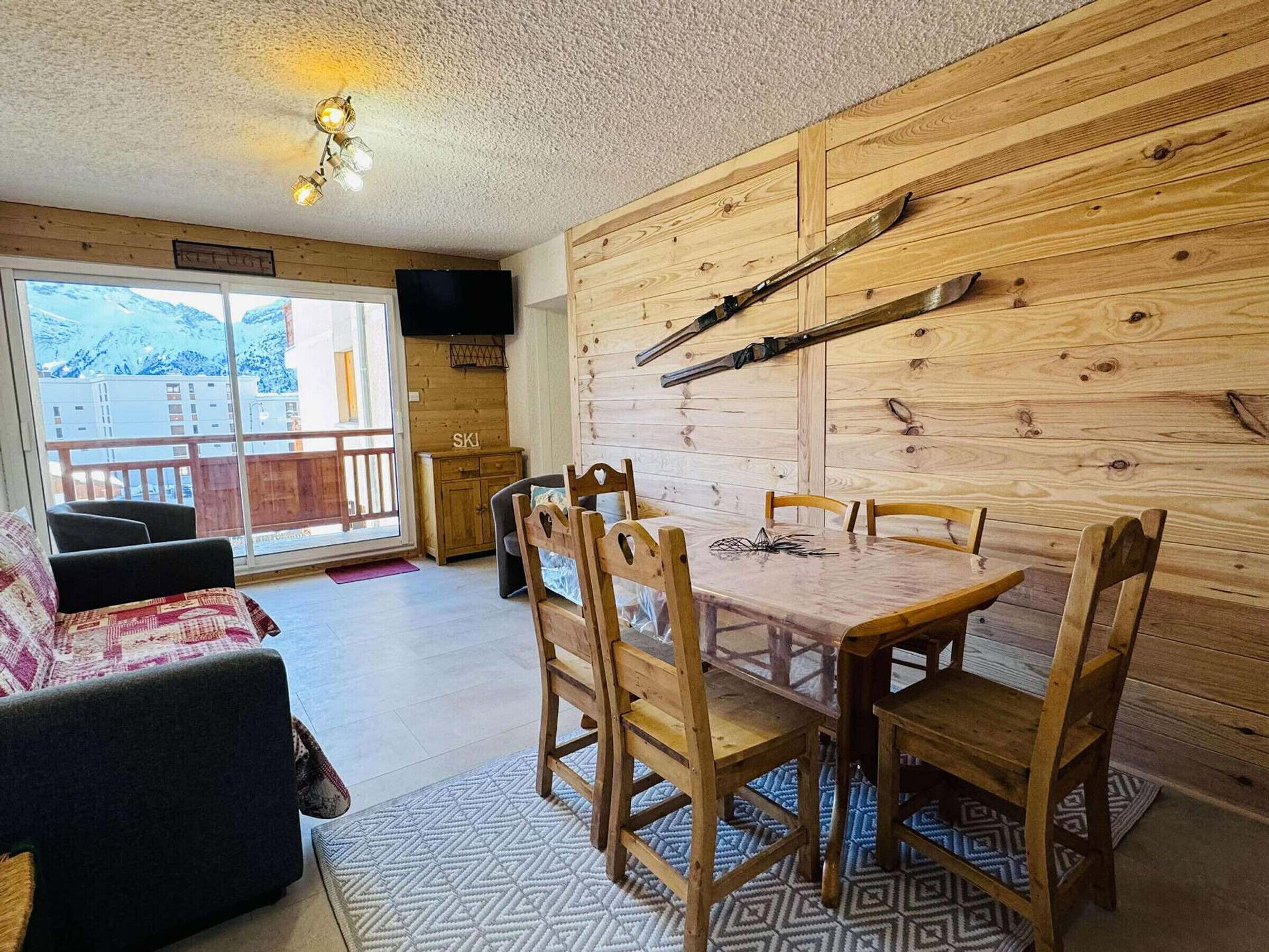 Un comedor con una mesa y sillas de madera, un televisor montado en la pared y vistas a montañas a través de un ventanal grande.