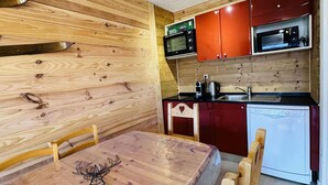A compact kitchen with wooden walls, a dining table with a deer design, and a microwave above the sink.