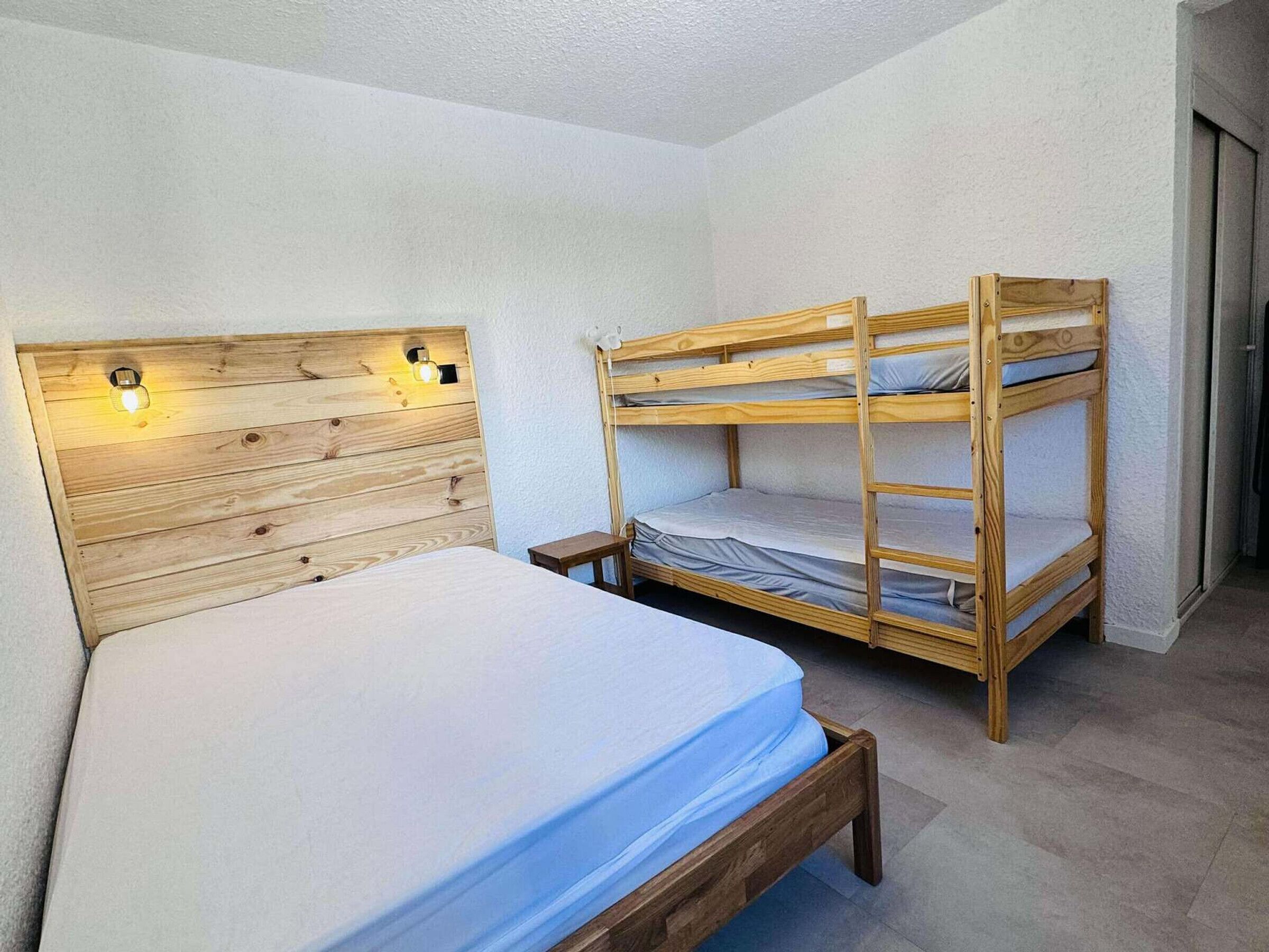 Una habitación con una cama litera de madera y una cama individual, ambas con ropa de cama blanca.