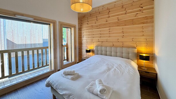 A bedroom with a large bed, wooden panel wall, two bedside lamps, and a view through a window. - Luxury chalet in Vars, comfort for 8 guests, private parking (Vars)