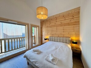 Une chambre à coucher avec un grand lit, un mur lambrissé en bois, deux lampes de chevet et une vue par la fenêtre.