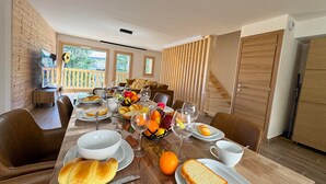 A dining area with a wooden table set for breakfast, including bread, fruit, and wine glasses. - Luxury chalet in Vars, comfort for 8 guests, private parking (Vars)