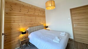 A bedroom with a wooden headboard, a bed with white bedding, two bedside lamps, and a hanging light fixture. - Luxury chalet in Vars, comfort for 8 guests, private parking (Vars)
