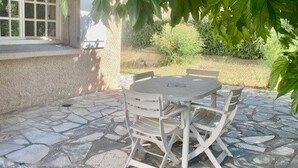 Une terrasse en pierre avec une table ronde et des chaises blanches.