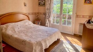Une chambre à coucher avec un lit en bois, une petite table de chevet, une fenêtre avec des rideaux et une vue sur la verdure à l’extérieur.